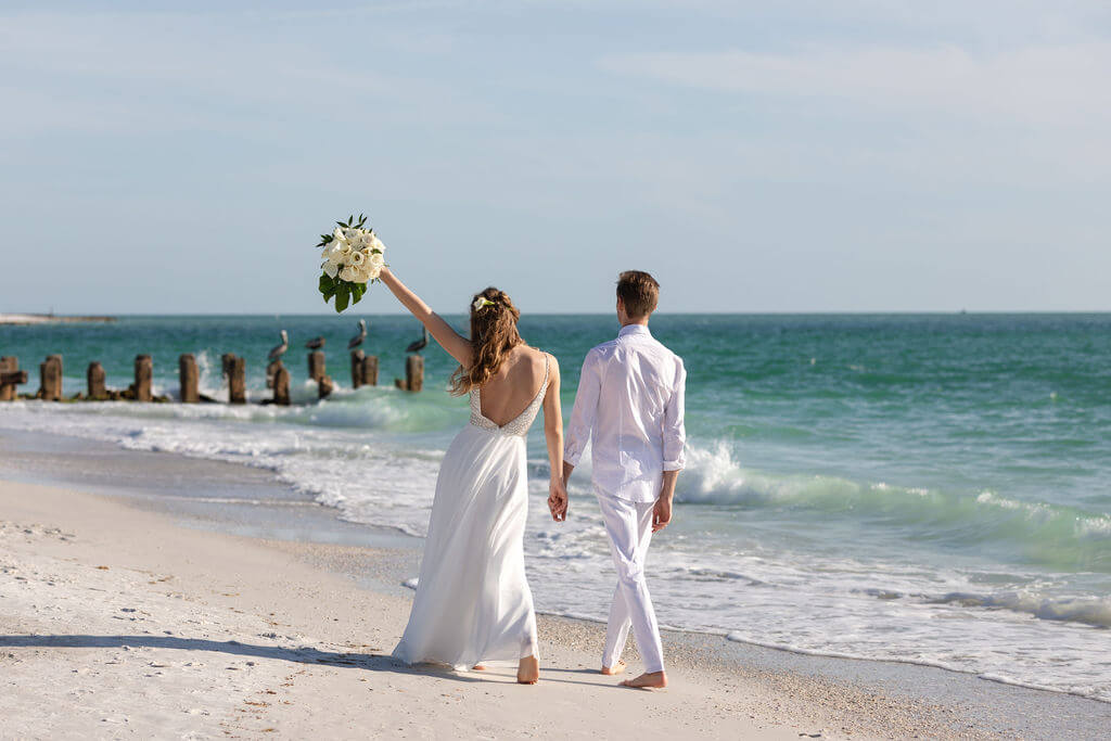 Bride and groom walking hand in hand to the Gulf on Anna Maria Island